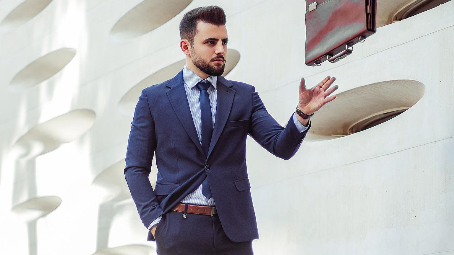 man in blue dress shirt and black pants standing near white wall